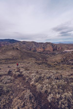 Hiker with backpack walking along rural road to cliff on gloomy day