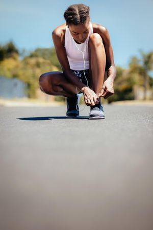 Fitness woman tying her shoelace on the road outdoors