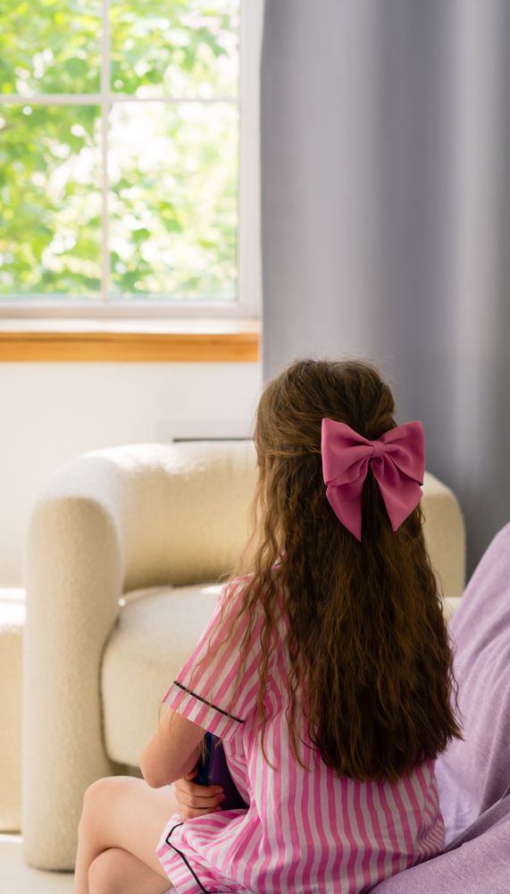 Girl with pink bow looking out a window