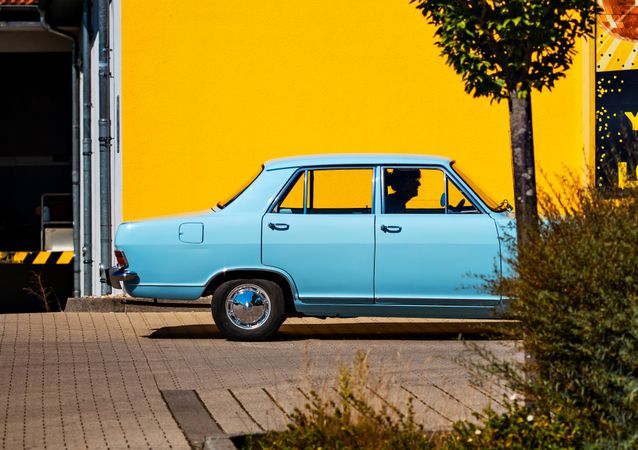 Sky blue retro car against a bright yellow wall. Color contrast.