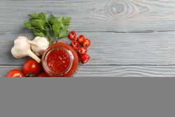 Jar with red chilli and tomato sauce, and spices on wooden table