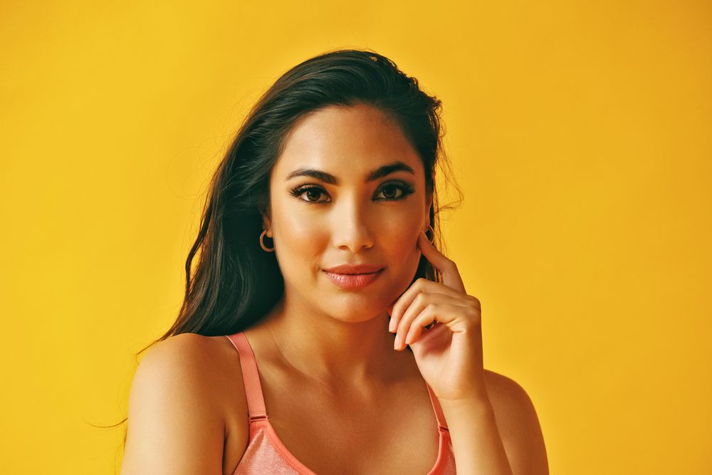 Headshot of curious Hispanic woman standing in front of a yellow background