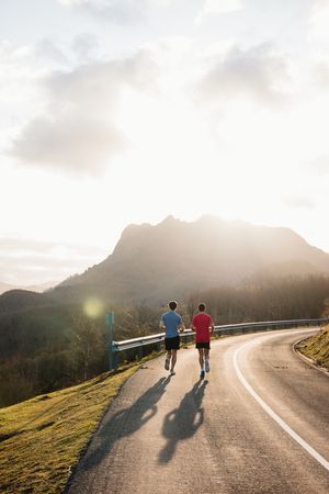 Sportsmen running on asphalt road in mountains