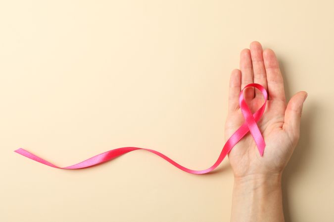 Female hand hold pink awareness ribbon on color background, space for text