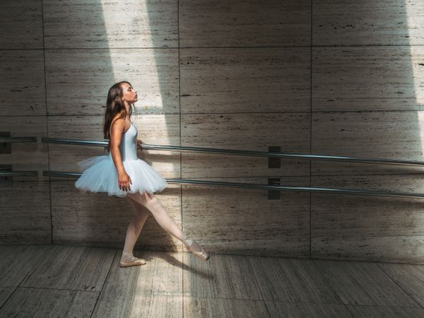 Ballerina doing ballet posing at rail in classroom