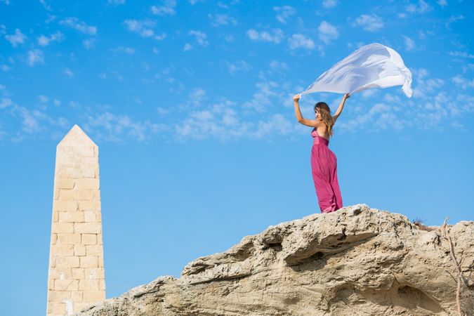 Woman in dress with scarf in upped hands near stone monument