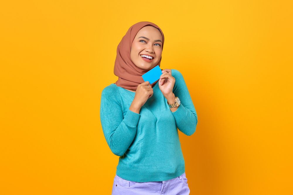 Muslim woman smiling while holding credit card with both hands