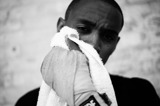 Greyscale photo of man wearing boxing gloves holding a towel