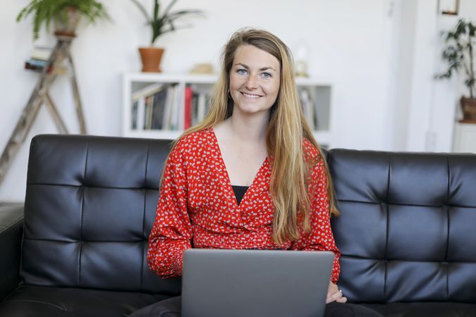 Smiling woman sitting on a sofa at home using a laptop