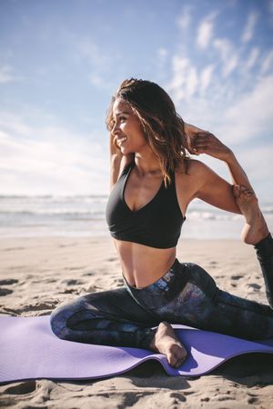 Happy young woman doing yoga exercise on beach