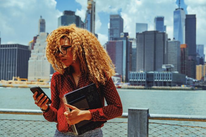 Serious professional Black female checking phone by Hudson River