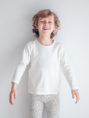 Boy in white pajamas leaning against the white wall of his house.
