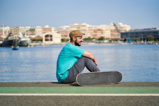 portrait of a young man with skateboard on a road next to the harbor in the morning