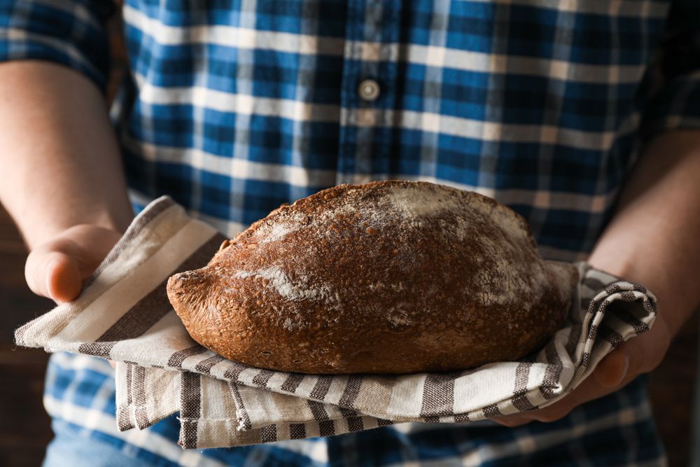 Male hands hold wheat bread against wooden background, space for text