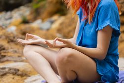 A young women practices yoga on the beach, with her hands and fingers in asana gesture