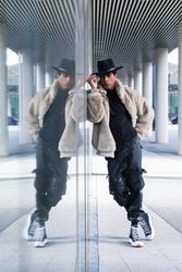 Stylish hispanic man reflecting in glass wall on street