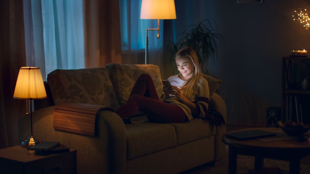 In the Evening Young Woman Lies on the Couch and Uses Smartphone.