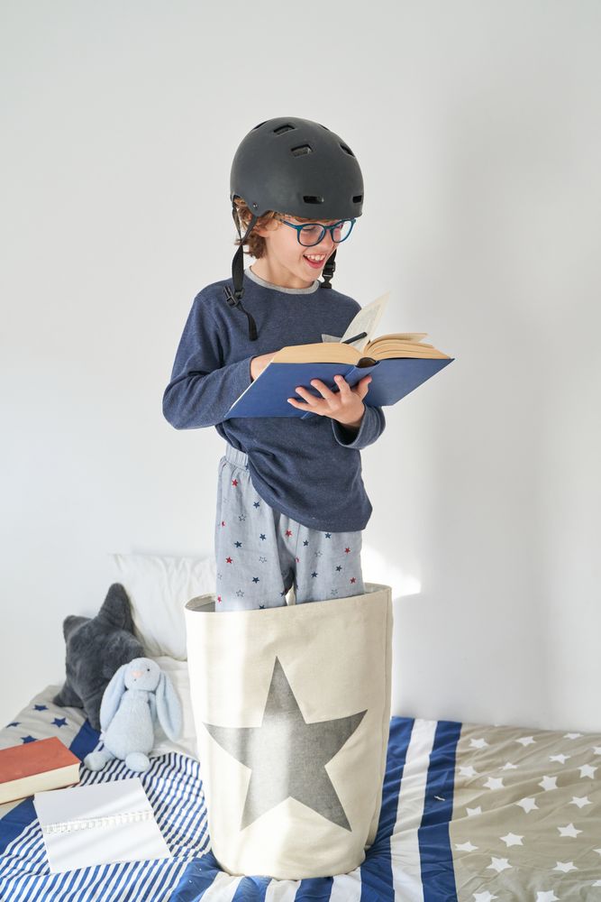Satisfied boy in helmet reading book in bedroom