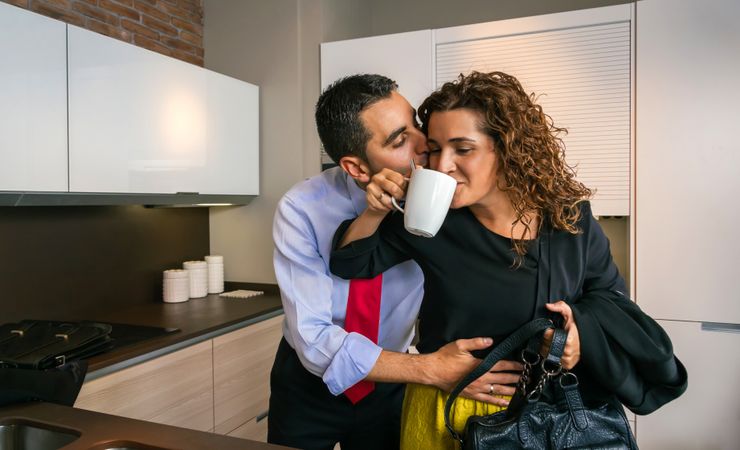 Businessman embracing and kissing woman while drinking fast cup of coffee before going to work