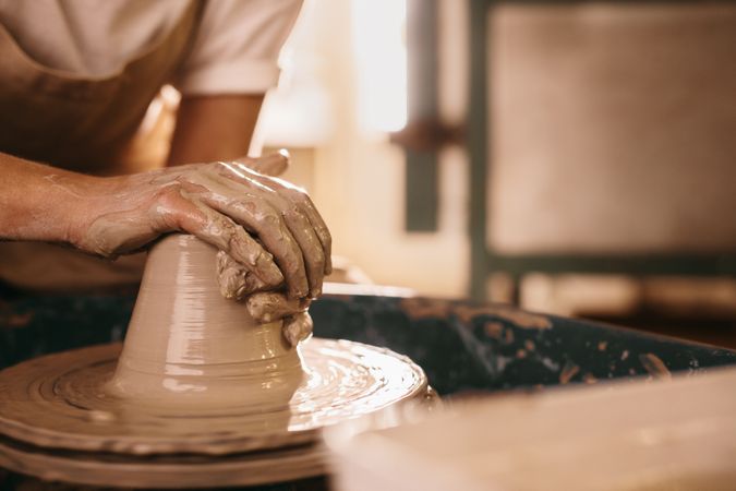 Potter moulding clay in hands on pottery wheel