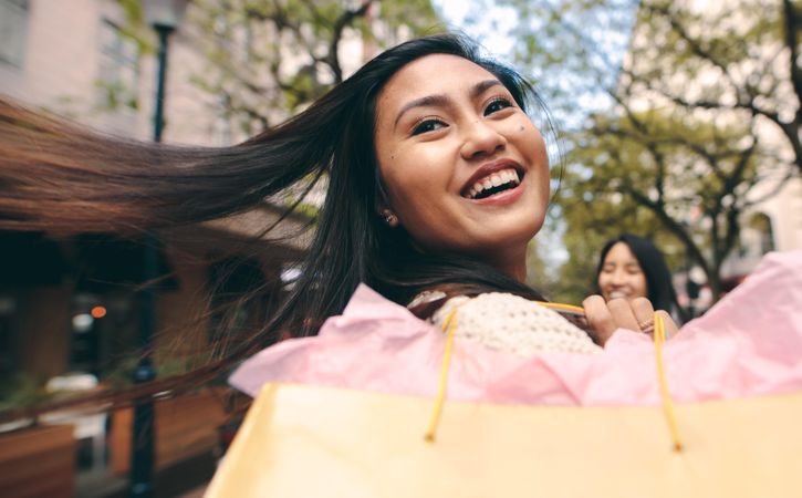 Happy young Asian woman tossing hair with shopping bag