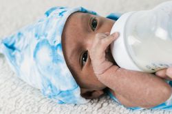Anonymous mother feeding newborn baby wrapped on soft blanket