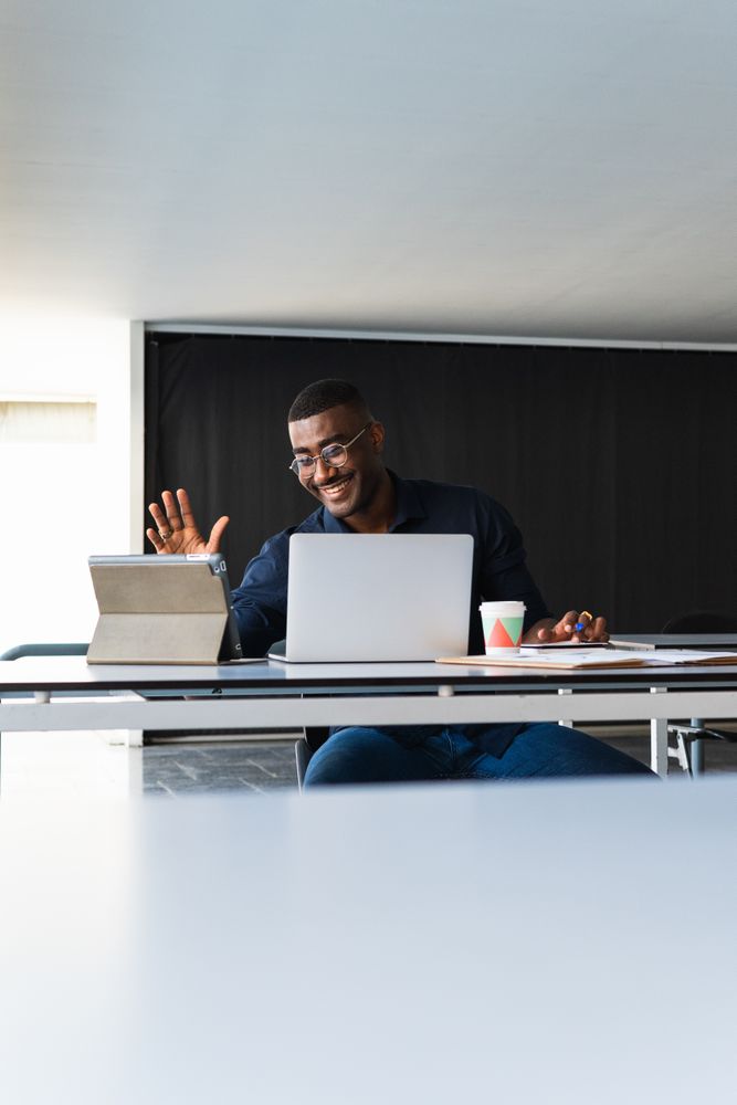 Black man video chatting on tablet near laptop in workplace