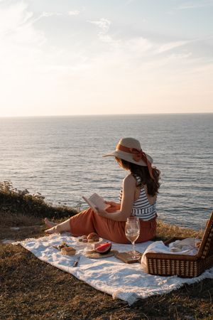 Woman reading on mat for picnic on seashore
