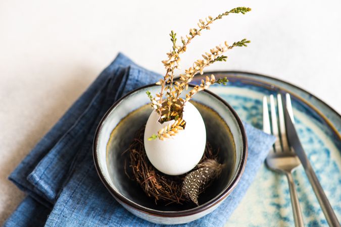 Decorative egg with plant and feather on blue napkin for Easter table setting