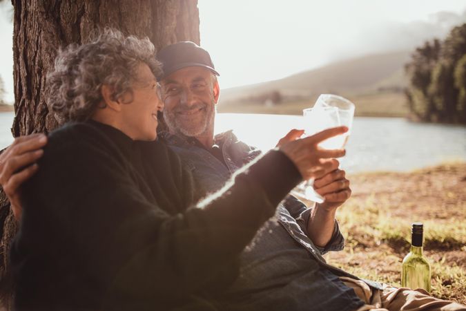 Portrait of relaxed mature couple sitting at a tree and toasting wine