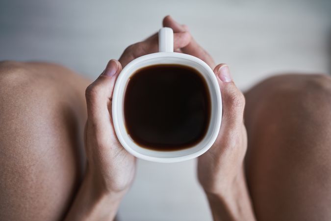 Faceless woman drinking coffee in room