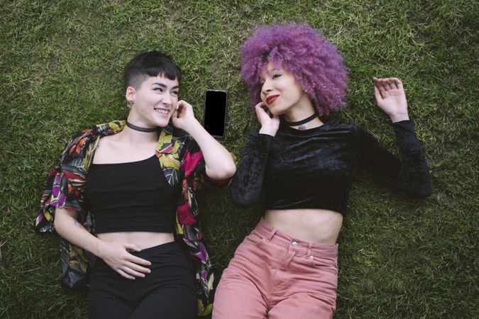 Women in colorful shirt and with pink hair lying on grass