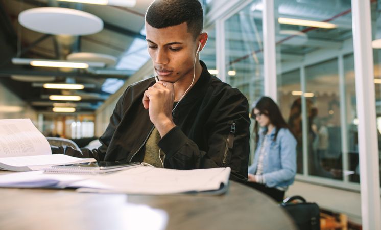 Man wearing earphones looking at digital tablet while sitting at university library
