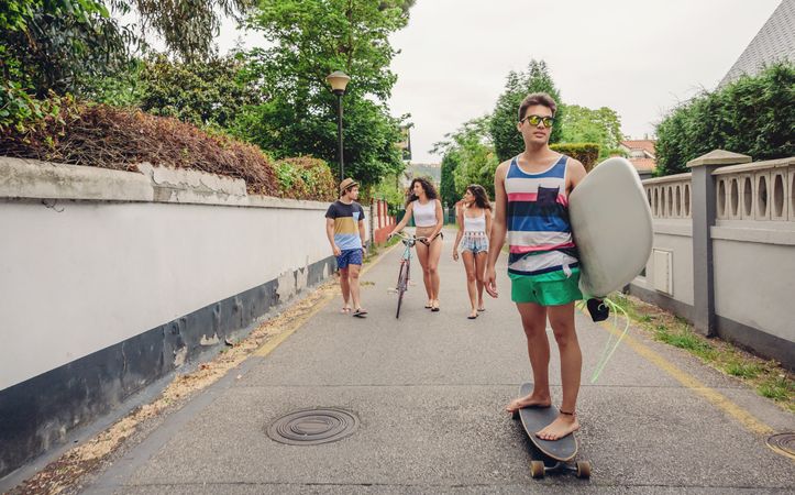 Young male riding on skate and holding surfboard