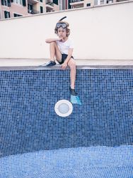 Sad preteen boy sitting on side of empty pool