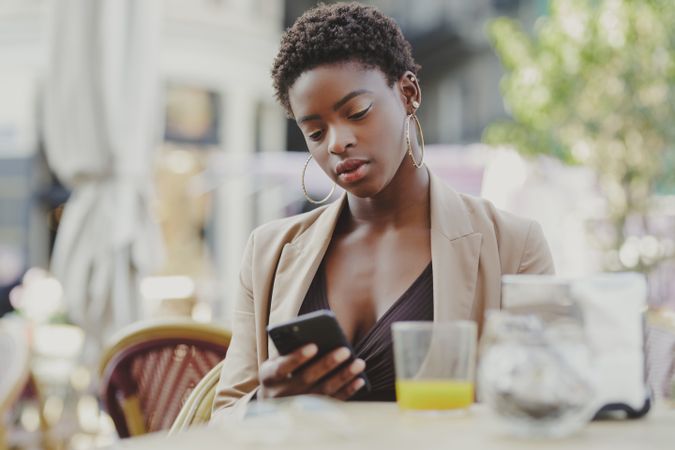 Smiling Black woman with smartphone sitting at table near luggage in cafe