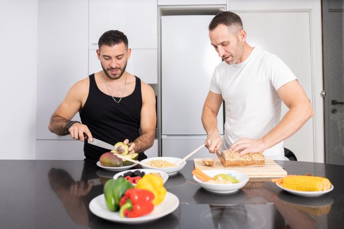 Male couple preparing vegetables and cutting bread for lunch