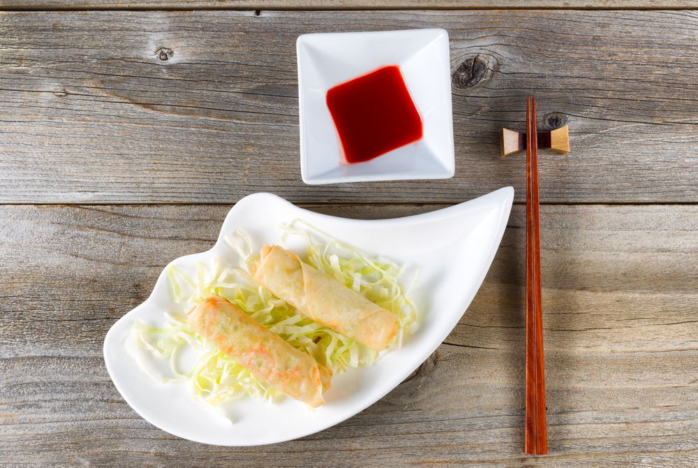 Fried Chinese spring rolls and sweet dipping sauce in bowl on rustic wood