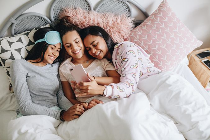 Young women taking selfie lying on bed during slumber party