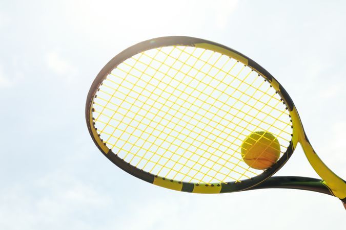 Tennis racquet with tennis ball against sky background