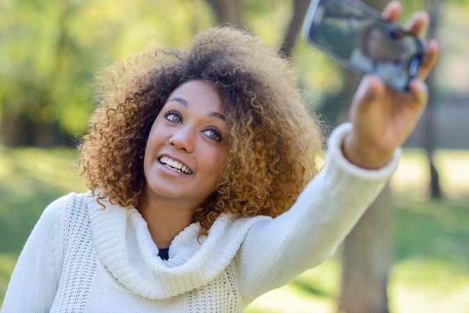 Happy Black woman taking a selfie on her phone in bright park