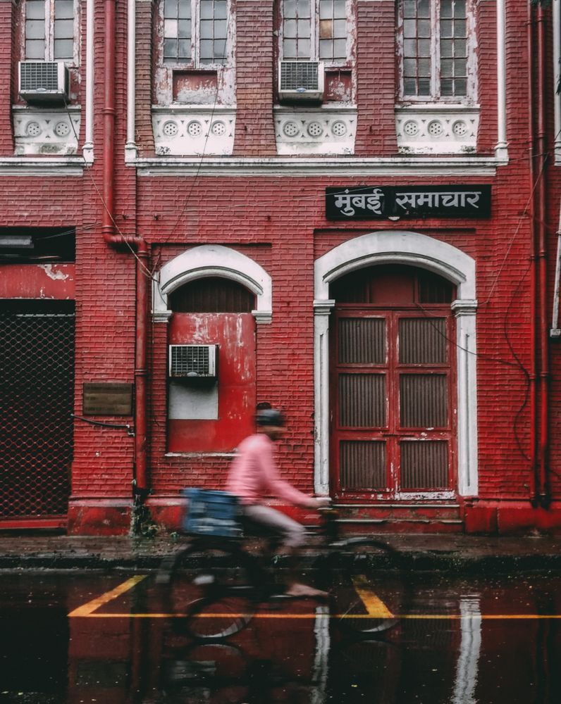 Side view of a person in pink shirt riding a bicycle beside red building