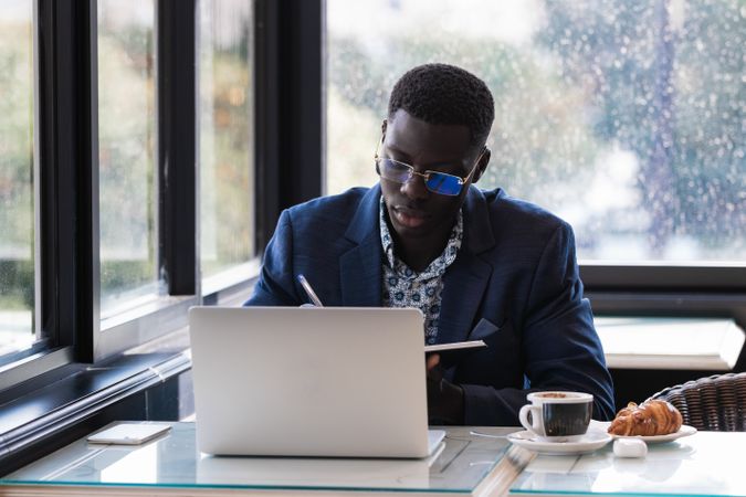 Focused Black male entrepreneur taking notes during work in cafe