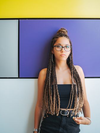 Charming teenage girl with braids in sunglasses nearby colorful wall