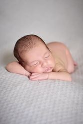 A naked newborn sleeping on her hands on top of a gray blanket