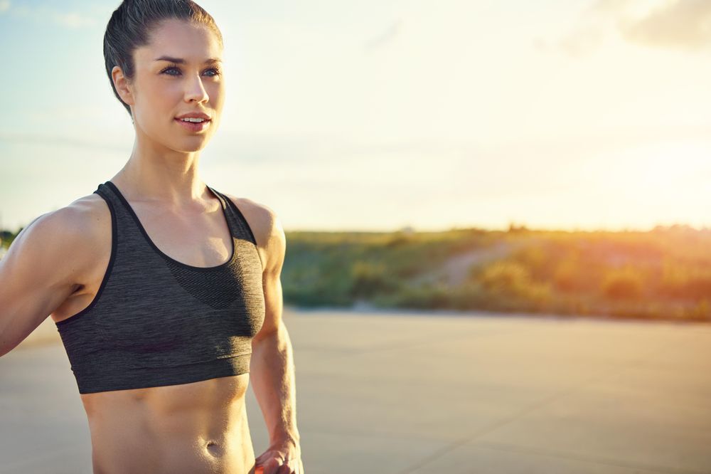 Muscular woman in sports bra lit in morning sunlight