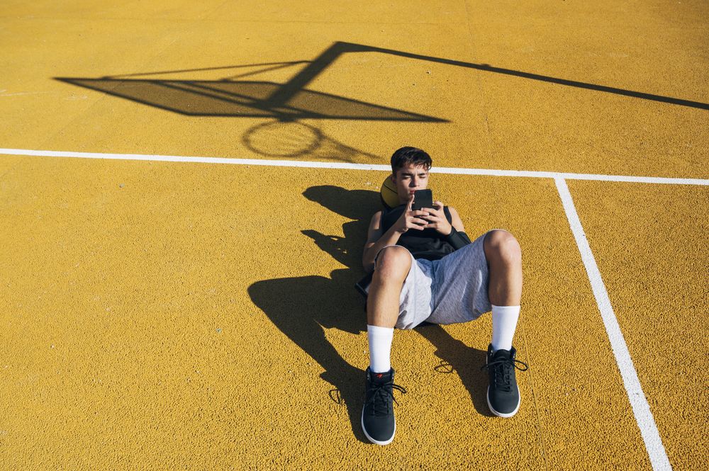 Male basketball player using his smartphone resting after training
