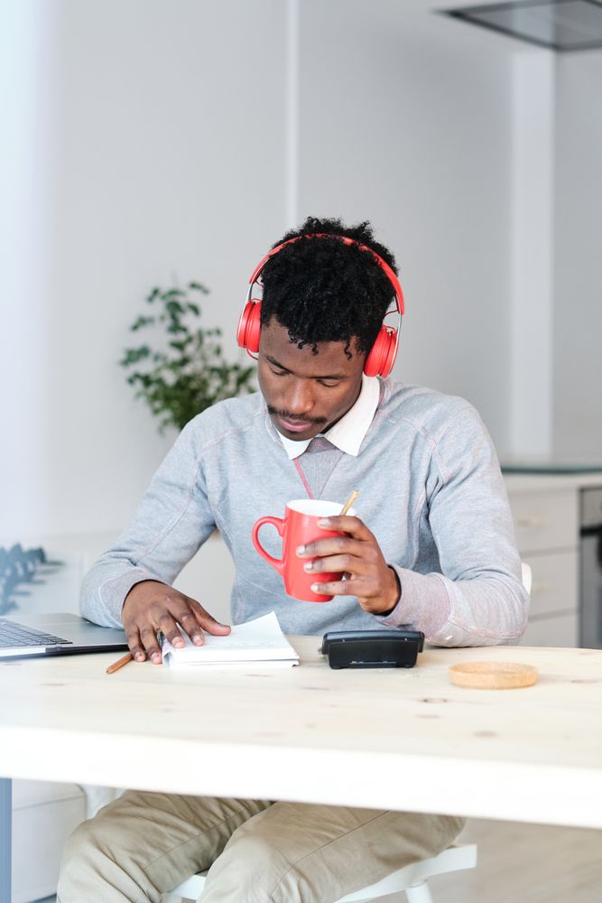 Tired Black economist in headphones with coffee working at home