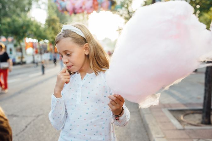 Cheerful girl eating cotton candy on street