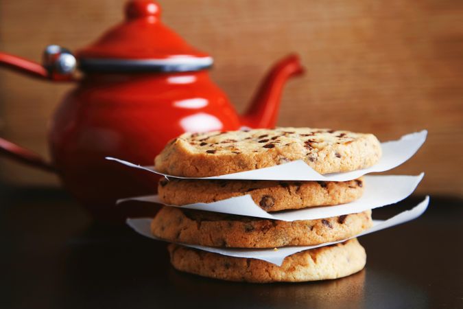Pile of cookies on wooden kitchen counter with red tea pot